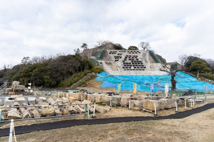 復旧工事の現場。斜面には地盤安全の安全率を上げるため、グラウンドアンカー工法が施されている（黒い四角板の箇所）。回収された石材は大小さまざまだが、間近で見ると大きく、迫力がある（写真手前）。